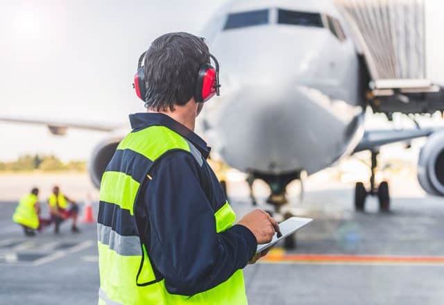 An airport worker on the ground looking at a commercial aircraft