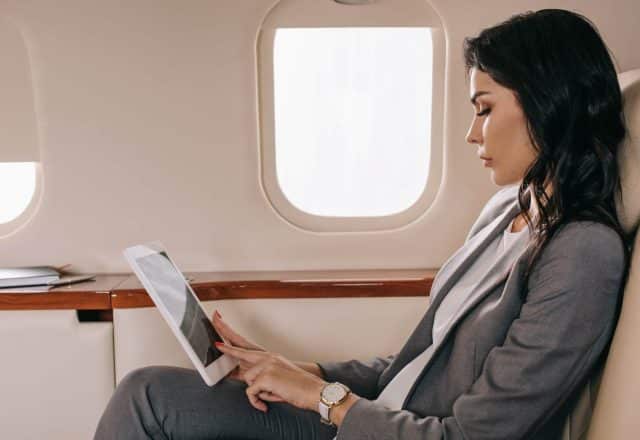 woman seated on private jet holding tablet