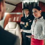 A private jet crew greets a passenger as they board the aircraft.