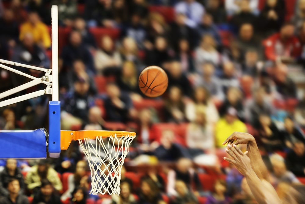 A basketball falls into the hoop against a backdrop of cheering fans in a stadium.