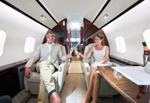 A happy couple toasts champagne while sitting in their private jet.