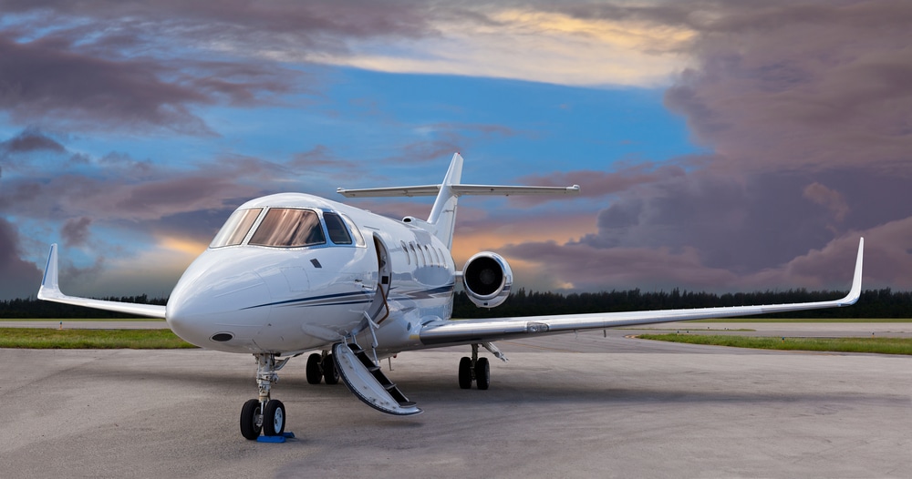 A private jet sits on the tarmac illuminated by a glowing sunset.