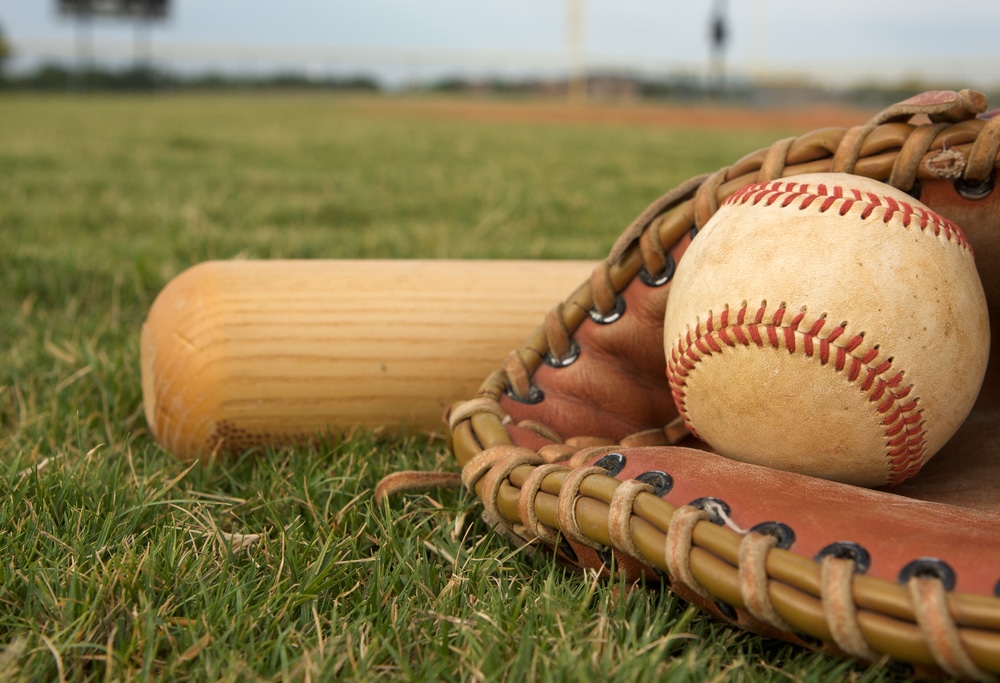 A baseball glove, ball and bat on the diamond.