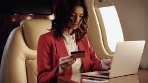 A woman flying on a private jet holding a credit card near a laptop.