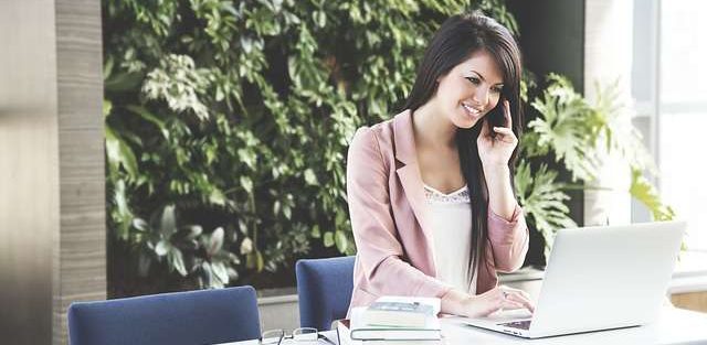 Woman in Pink Blazer on Phone in Front of Laptop | Stratos Jet Charters, Inc.