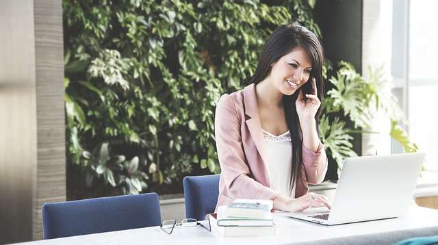 Woman in Pink Blazer on Phone in Front of Laptop | Stratos Jet Charters, Inc.